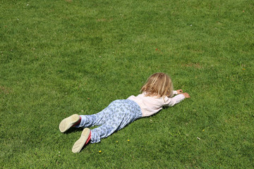 little blond girl lying on grass during summer holidays