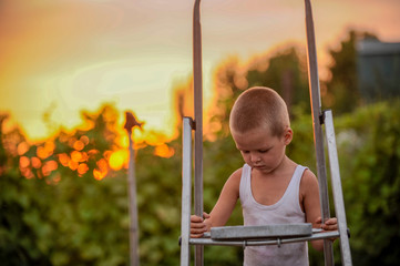 Rustic boy in white T-shirt in farmyard on background of sunset. child is happy in village on vacation
