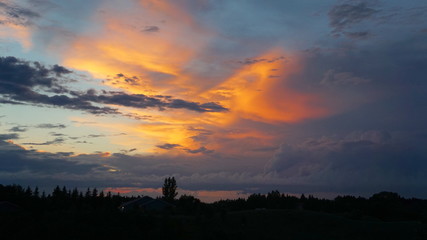 Fototapeta premium Lakeside blazing sunset bold sky with colored clouds treed shoreline 