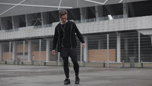 Attractive male athlete does morning exercise outdoors close up slow motion in the cloudy weather. Workout standing on the street near sports stadium. Healthy lifestyle will power motivation concept.