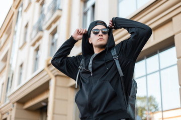 Modern young handsome hipster man in a fashionable sweatshirt with stylish sunglasses in a cap with...