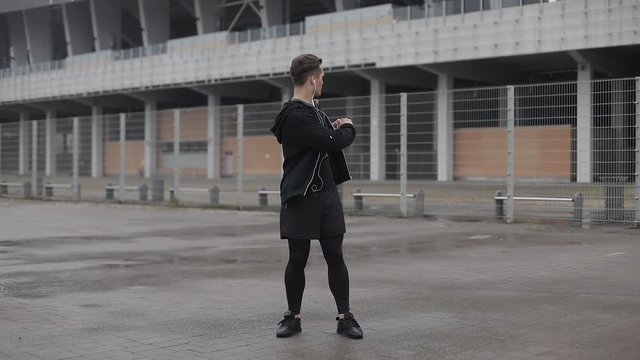 Attractive male athlete does morning exercise outdoors close up slow motion in the cloudy weather. Workout standing on the street near sports stadium. Healthy lifestyle will power motivation concept.