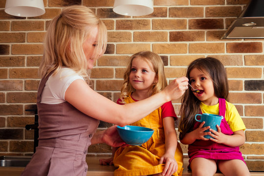 Mother feeding two daughters in the kitchen sitting on the table