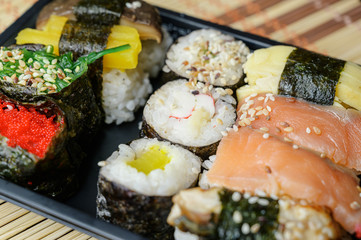 Set of various rolls in black plastic box. Rolles collection with crab sticks, salmon, sockeye salmon, coho salmon, masago caviar, wakame, shiitake mushrooms, eel, radish, nori seaweed.