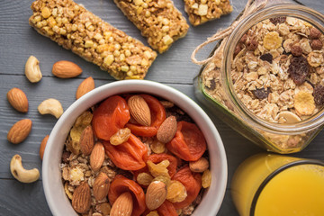 Granola cereal flakes with dried fruit, nuts in green bowl on gray wooden table. Top view.
