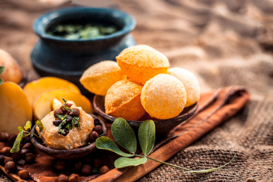 Famous Indian & Asian street food dish i.e. Panipuri snack in a clay bowl along with its flavored spicy water in another clay vessel. Entire consisting raw ingredients present on the surface.