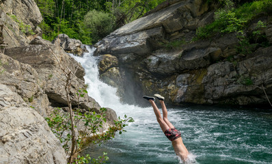 Young man diving in a natural pool in front a waterfall