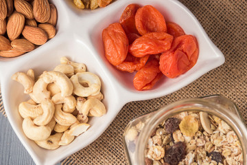 Granola cereal flakes with dried fruit, nuts in bowl on gray wooden table. Top view.