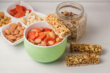 Granola cereal flakes with dried fruit, nuts in green bowl on white wooden table.