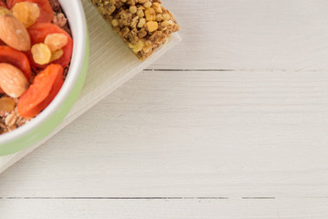 Granola cereal flakes with dried fruit, nuts in green bowl on white wooden table. Top view with copyspace.