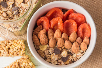 Granola cereal flakes with dried fruit, nuts in green bowl on white wooden table. Top view.