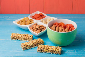 Granola cereal flakes with dried fruit, nuts in green bowl on blue wooden table.