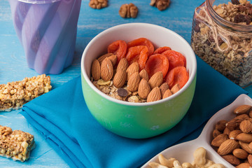 Granola cereal flakes with dried fruit, nuts in green bowl on blue wooden table.