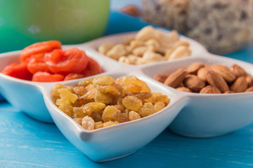 Granola cereal flakes with dried fruit, nuts in plate on blue wooden table.