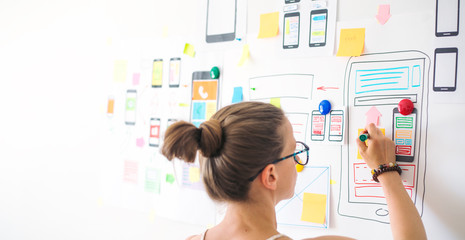 A young female designer is developing a web application for mobile phones. Woman draws a mockup of...
