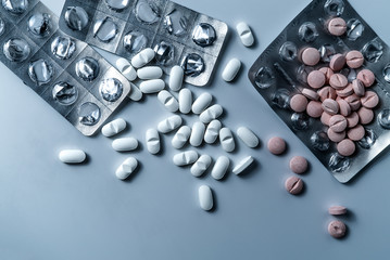 Top view of many prescription drugs, medicine tablets or vitamin pills in a pile and empty blister packs on clean white background in blue color tone - Concept of healthcare, opioids addiction