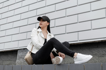 Pretty young woman in a stylish leather jacket in a t-shirt in black jeans in white sneakers in a...