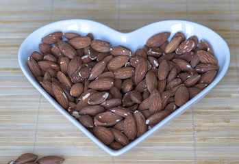 Nuts arranged in heart  on background. Healthy Food image close up almond on the cup plate. Love Texture on top view mock up