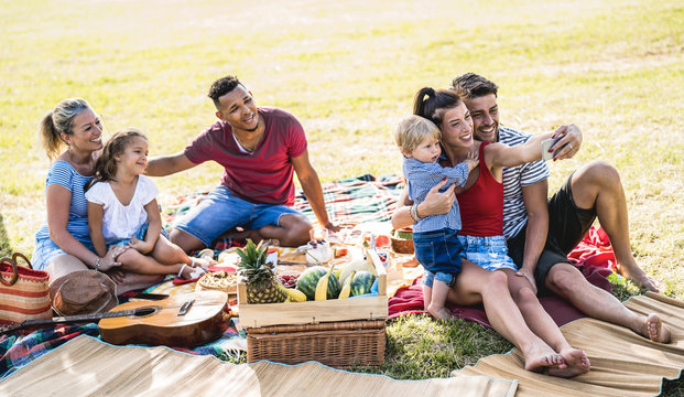 Happy multiracial families taking selfie at pic nic garden party - Multicultural joy and love concept with mixed race people having fun together picnic barbecue before sunset - Warm bright filter