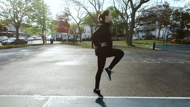 Woman Doing Leg Warming up Before Running in Morning. Young Fitness Girl Runner Jumping on playground. 4K
