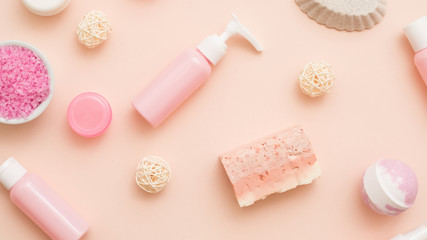 Beauty treatment. Flat lay of bath salt, handmade soap, cosmetic jars and lotion bottles over peach color background.