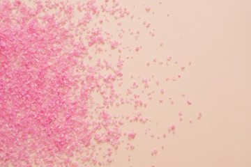 Pink bath salt crystals scattered on peach color surface. Abstract background. Spa therapy.