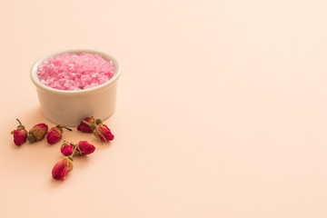 Obraz na płótnie Canvas Spa aroma therapy. Closeup of pink bath salt in white bowl and red rose flower buds. Peach background. Copy space.