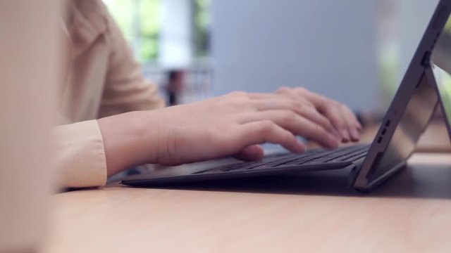 Close up female hand typing on laptop keyboard on wooden table in classroom
