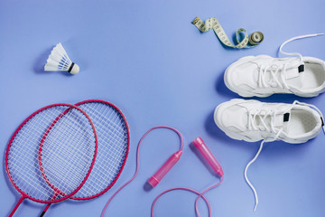 Sports flat lay with shuttlecock and badminton racket, skipping rope, sneakers and measuring tape on purple background. Fitness, sport and healthy lifestyle concept.