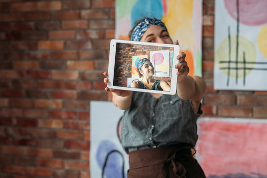 Creative Blogger. Talented Female Artist Uisng Tablet To Take Selfie With Her Artworks In Studio. Blur Background. Copy Space.