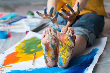 Fun leisure. Cropped shot of artist sitting on floor, showing feet and hands dirty with multicolor...