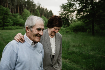 Happy smiling senior couple in love on nature, having fun. Elderly couple on the green field. Cute senior couple walking and hugging in spring forest