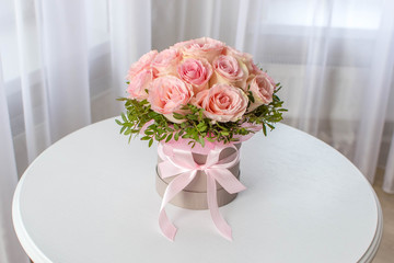 Beautiful bouquet of pink roses in a festive round box on a white table. Gift for holiday, birthday, Wedding, Mother's Day, Valentine's day, Women's Day.  Flowers in a hat box.
