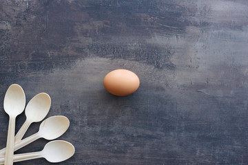 Top view of egg in the middle of background of marble kitchen counter. Natural wooden spoons in the corner. Copy space.