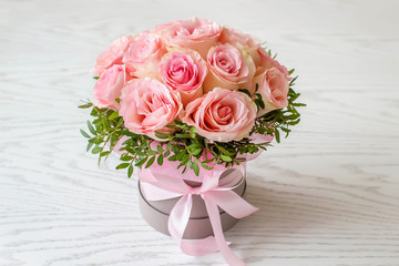 Beautiful bouquet of pink roses in a festive round box on a white table. Gift for holiday, birthday, Wedding, Mother's Day, Valentine's day, Women's Day.  Flowers in a hat box.