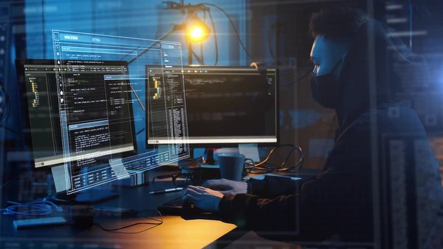 cybercrime, hacking and technology concept - asian male hacker in mask writing code or using computer virus program for cyber attack at dark room