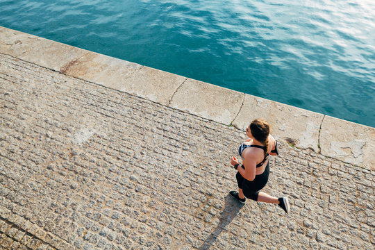 Plus size woman running at seaside on a pier. - Powered by Adobe