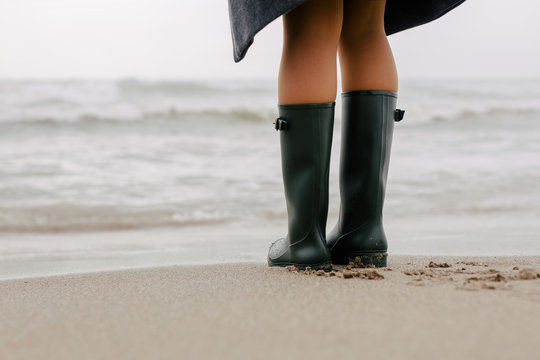 Closeup of a woman wearing gumboots on the beach.