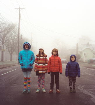 Four kids in height order standing in a street on a foggy morning in Portland, Oregon.