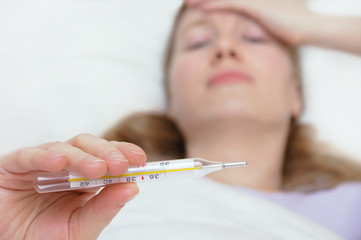 Cold and headache. Caucasian girl is lying in bed with a thermometer in her hand.
