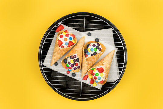 Delicious ice cream with candies and fruits on a grill against a yellow background
