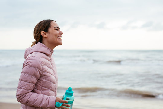 Active woman drinking water after workout on the beach.