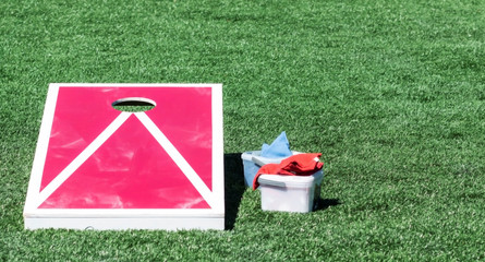 Red and white cornhole board with bean bags in container