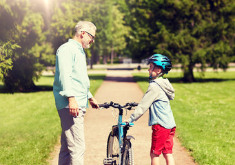 family, generation, safety and people concept - happy grandfather and boy with bicycle and bike helmet talking at summer park