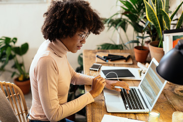 Afro businesswoman working in office full of plants.