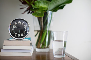 Bedside table with vintage analogue alarm clock, books, water and vase