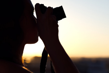 Silhouette of girl photographer taking picture on compact camera on the sunset background.