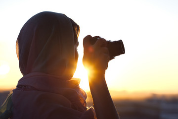Arab Woman Photographer in a scarf taking picture using Camera on the sunset background. Halal...