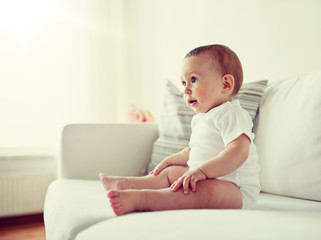 childhood, babyhood and people concept - happy little baby boy or girl sitting on sofa at home