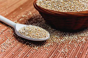 White seeds of Quinoa in a wooden spoon and a wicker bowl. Healthy nutrition and superfoods. Latin name Chenopodium quinoa. Food for gluten-free diet. Food for vegetarians and vegans. 